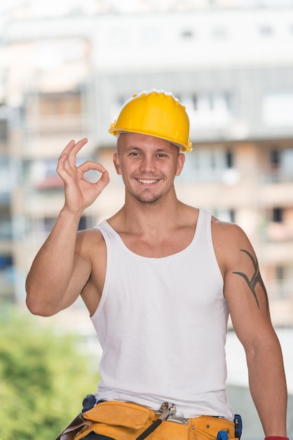 Retrato de um trabalhador da construção civil com capacete amarelo fazendo sinal de polegar para cima