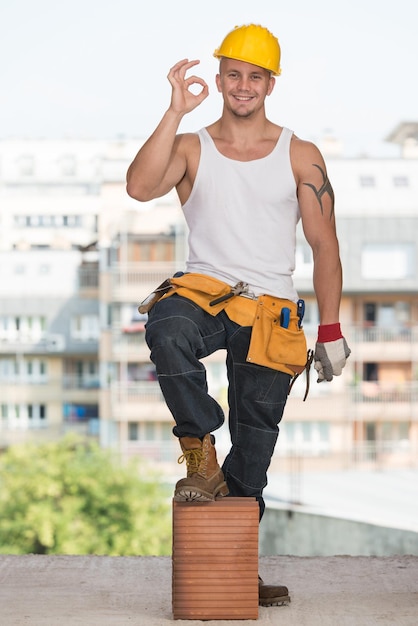 Foto retrato de um trabalhador da construção civil com capacete amarelo fazendo sinal de polegar para cima