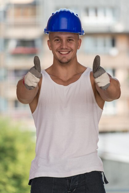 Foto retrato de um trabalhador da construção civil com capacete azul fazendo sinal de polegar para cima