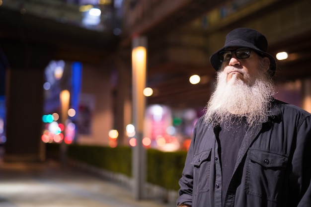 Retrato de um turista barbudo maduro explorando as ruas da cidade de bangkok, na tailândia, à noite