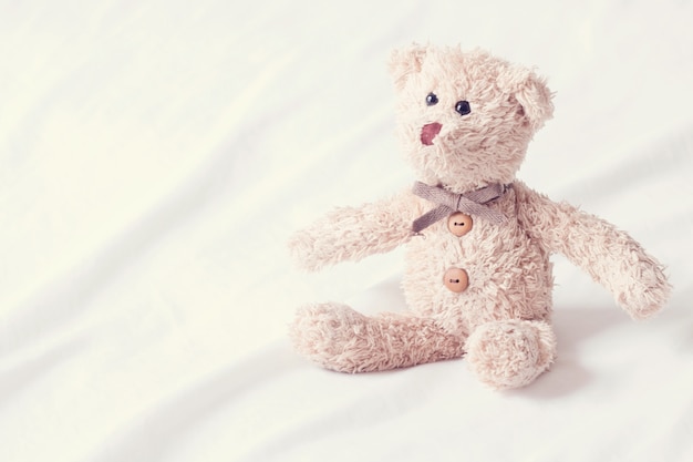 Retrato de um ursinho de ursinho feliz e atraente sorrindo, urso de pelúcia bonito deitado no fundo de tecido branco.