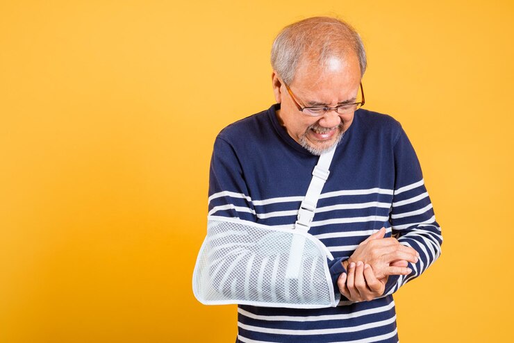 Foto retrato de um velho asiático lançado em seu braço emoções dolorosas tirado em estúdio isolado fundo amarelo homem idoso aposentado após acidente braço quebrado usar talha de braço para tratamento