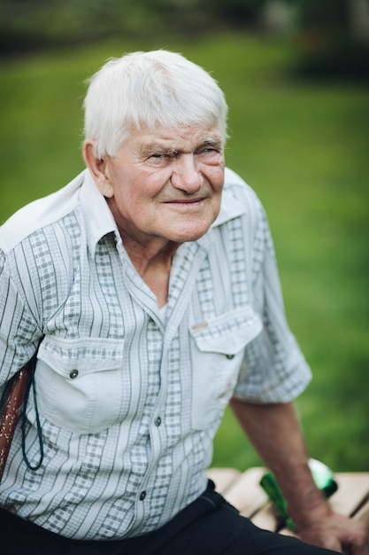 Retrato de um velho avô caucasiano com cabelo loiro na camisa branca, sentado em um banco, sorrindo e curtindo sua vida