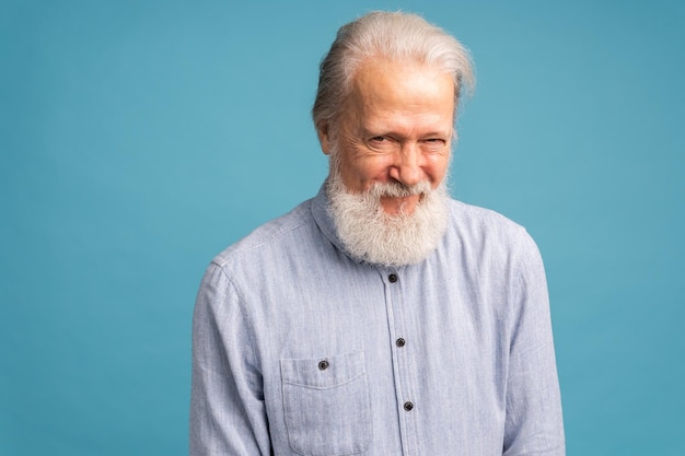 Retrato de um velho de barba branca que usa camisa azul clara sobre fundo de cor azul, emoções humanas positivas, sentimentos de expressão facial