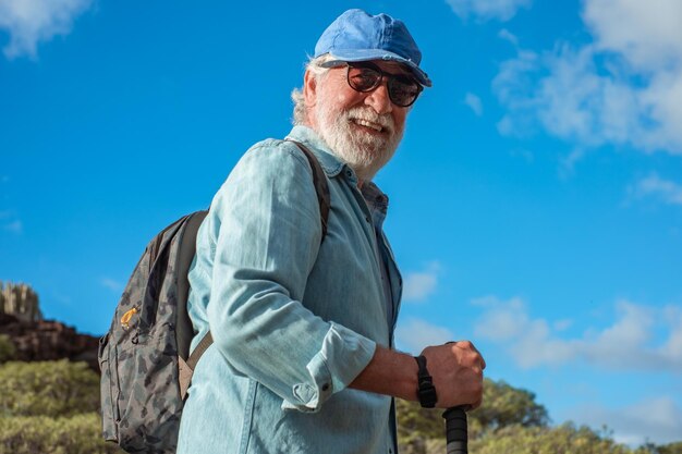 Retrato de um velho sorridente sênior com chapéu desfrutando de um dia de caminhada caminhando no céu azul da natureza