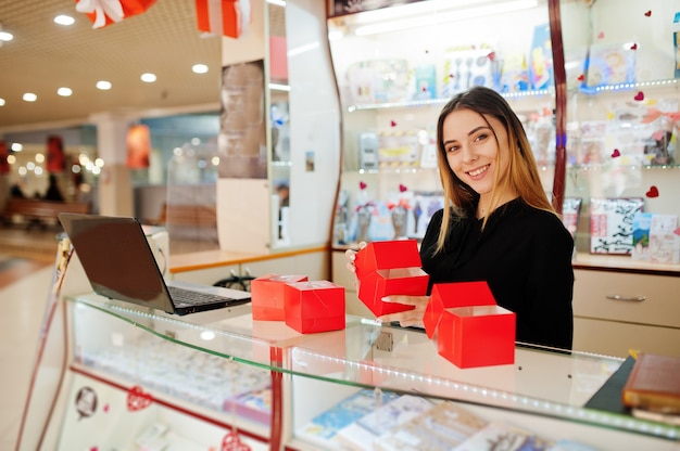 Retrato de um vendedor de jovem mulher branca segurando caixas de presente vermelhas. Pequena empresa de loja de lembranças de doces.