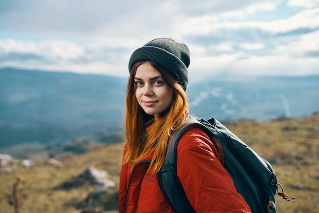 Retrato de um viajante em uma jaqueta vermelha e chapéu e com uma mochila ao ar livre nas montanhas ar fresco