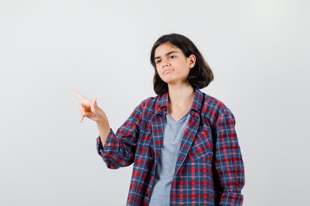 Retrato de uma adolescente apontando para o canto superior esquerdo, desviando o olhar com roupas casuais e uma vista frontal sombria