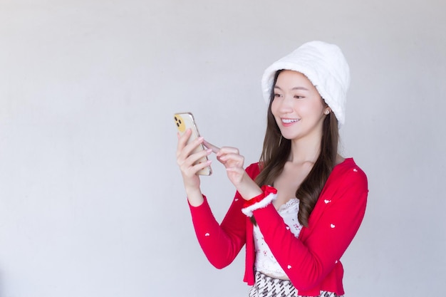 Retrato de uma adolescente asiática com um vestido vermelho e um chapéu branco feliz usando um smartphone