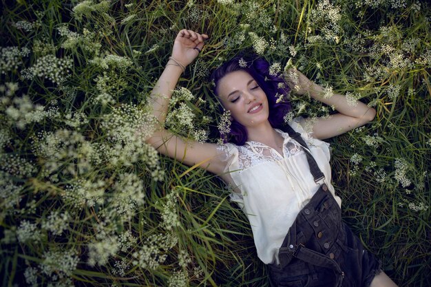 Retrato de uma adolescente com cabelo roxo e um brinco no nariz deitada na grama na natureza