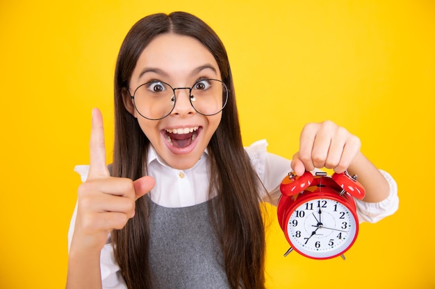 Retrato de uma adolescente com hora do relógio alrm e prazo Foto de estúdio isolada em fundo amarelo Menina adolescente surpreendida