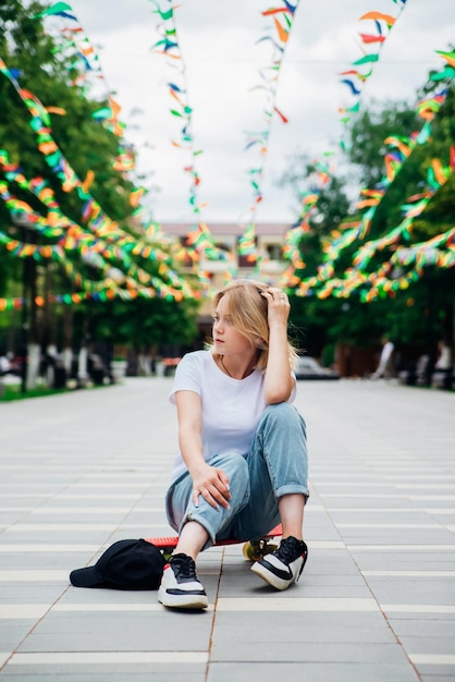 Retrato de uma adolescente em roupas casuais no parque estilo de vida ativo de skate de verão um estudante ou estudante está sentado em um skate durante as férias de verão recreação esportiva