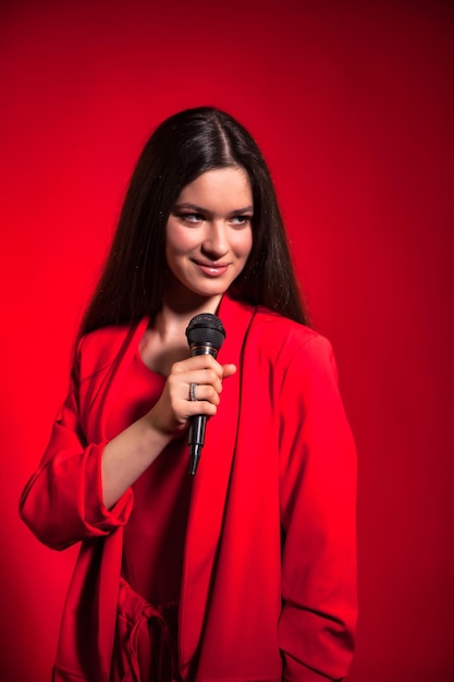Retrato de uma adolescente em traje vermelho elegante sobre fundo vermelho com microfone olhando para longe