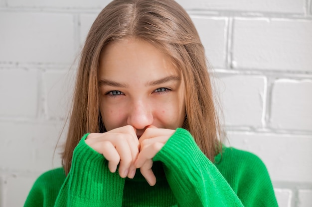 Retrato de uma adolescente esbelta em um suéter verde em luz natural contra uma parede de tijolos brancos. beleza natural, sem maquiagem. pele problemática. espaço para texto. Foto de alta qualidade