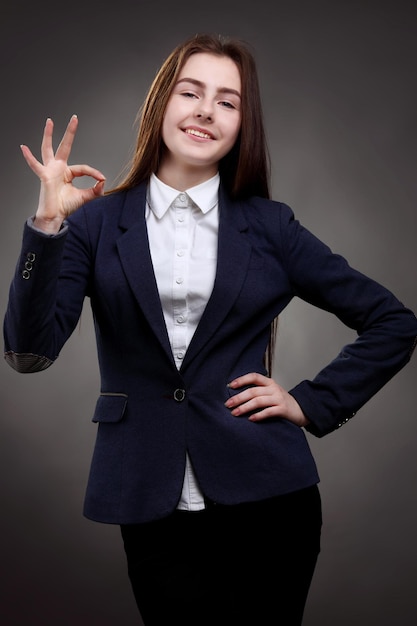 Retrato de uma adolescente feliz e boa colegial de camisa branca no estúdio de fundo cinza