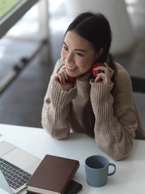 Retrato de uma adolescente feminina de suéter com fone de ouvido relaxando no espaço de trabalho