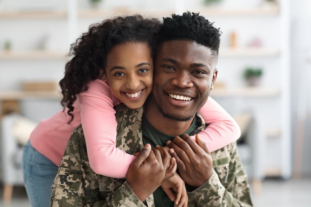 Retrato de uma adolescente negra alegre abraçando seu pai soldado