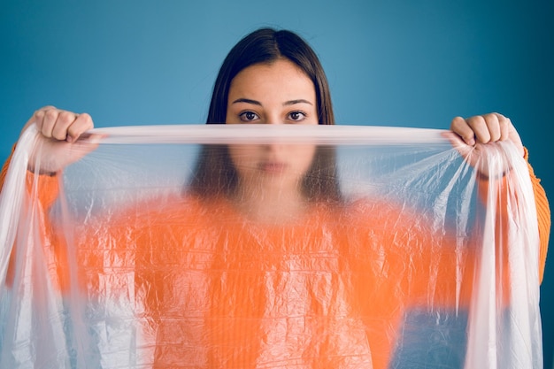 Foto retrato de uma adolescente segurando plástico enquanto está de pé contra um fundo azul
