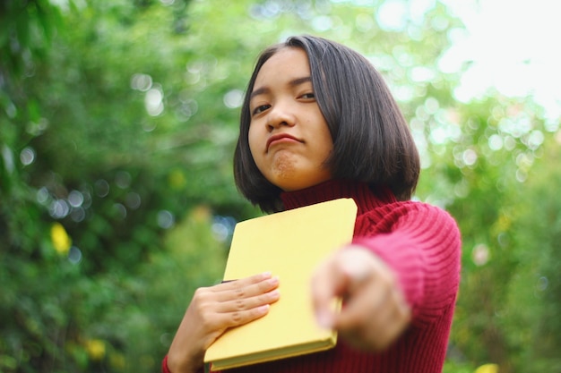 Foto retrato de uma adolescente segurando um livro apontando para o ar livre