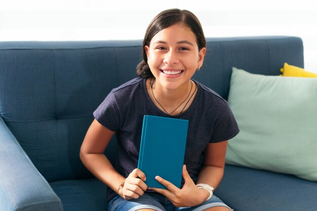 Retrato de uma adolescente sentada no sofá sorrindo, olhando para a câmera, ensino à distância