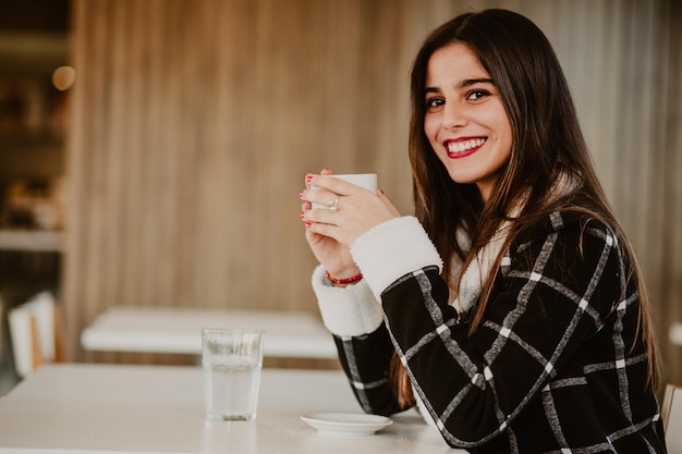 Retrato de uma adolescente sorridente com cabelos longos sentada em uma mesa em um café