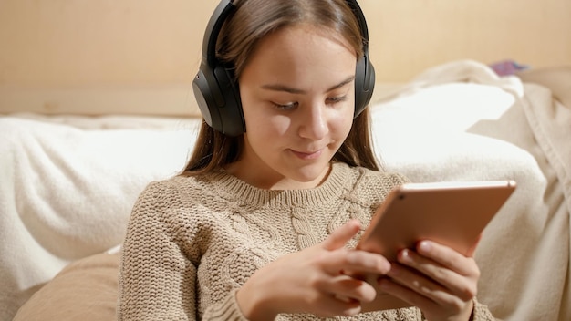 Foto retrato de uma adolescente sorridente com fones de ouvido usando um tablet e navegando na internet