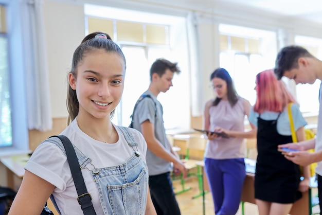 Foto retrato de uma adolescente sorridente na aula no intervalo. grupo de fundo de professores e colegas adolescentes falantes. escola, faculdade, estudo, conceito de juventude