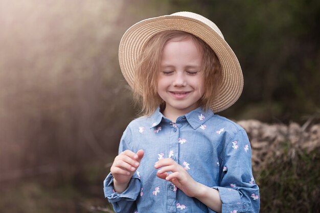 Retrato de uma adorável garota caucasiana de 5 anos de pé ao lado de uma árvore caída com raízes arrebentadas na floresta e olhando para o lado