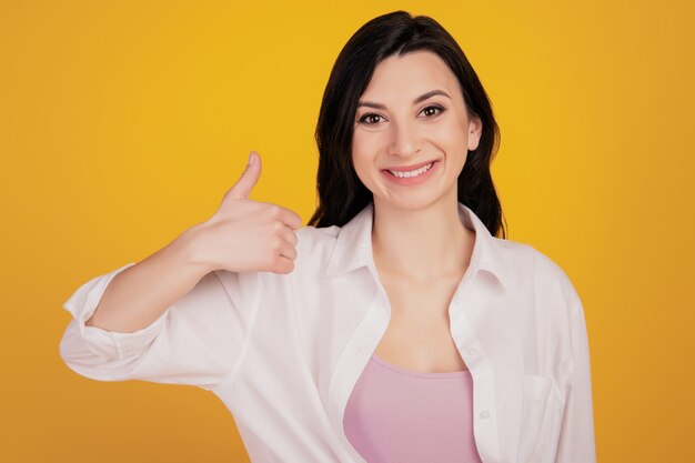 Retrato de uma adorável garota positiva levantando o polegar sobre fundo amarelo