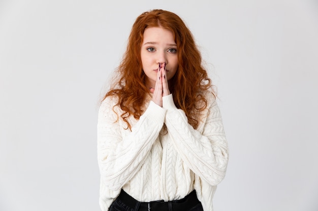 Retrato de uma adorável jovem ruiva em pé isolado sobre um fundo branco, orando