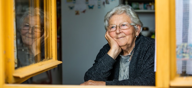 Retrato de uma adorável mulher sênior ou avó olhando pela janela e sorrindo