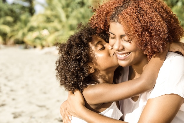 Retrato de uma alegre garota afro-americana beijando uma jovem mãe negra sorridente em dia de sol