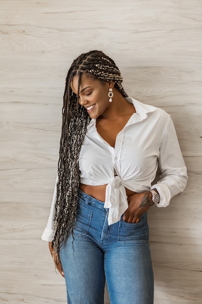 Foto retrato de uma alegre mulher adulta afro-americana em pé com o braço sobre o corpo e olhando para o lado. mulher adulta com tranças pretas e amarelas, posando no fundo de uma parede.