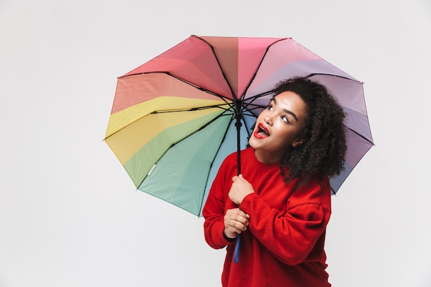 Retrato de uma alegre mulher africana isolada sobre um fundo branco, segurando um guarda-chuva colorido
