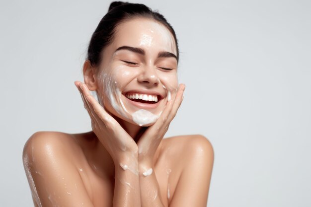Retrato de uma alegre mulher rindo aplicando espuma de limpeza para lavar o rosto linda morena com uma