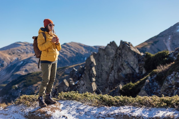 Retrato de uma alpinista de pé com uma xícara de chá na encosta do cume da montanha contra montanhas
