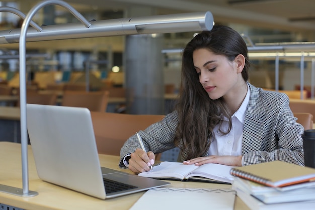 Foto retrato de uma aluna bonita com o laptop na biblioteca.