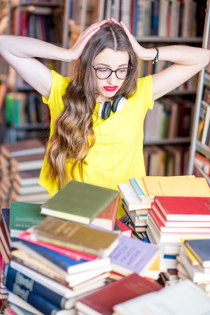Retrato de uma aluna cansada e estressada estudando com livros na biblioteca