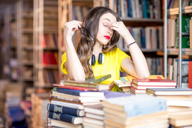 Retrato de uma aluna cansada estudando com livros na biblioteca