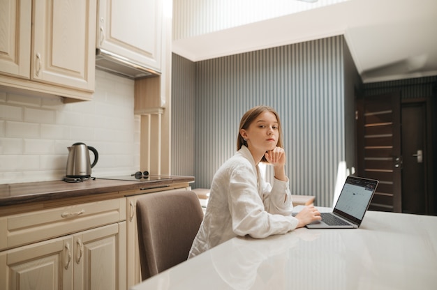 Retrato de uma aluna sentada em uma mesa na cozinha e usando um laptop