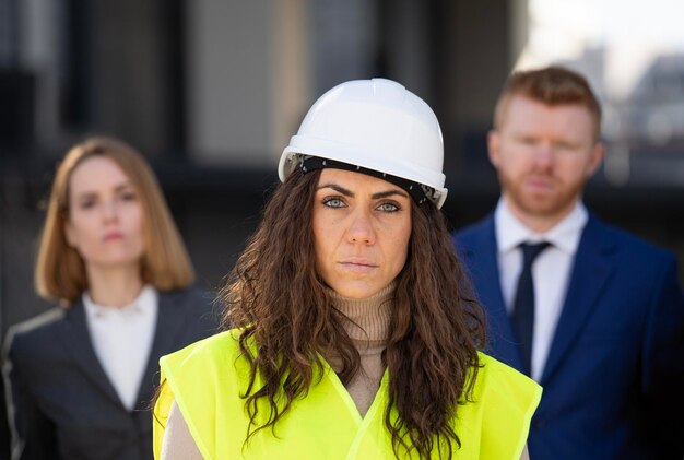 Retrato de uma arquiteta de construção mulher séria com executivos de clientes por trás de uma empresa de liderança feminina