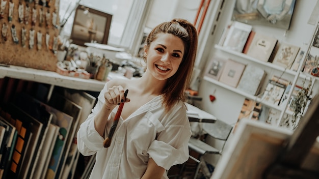 Retrato de uma artista feminina sorridente feliz com pincel na oficina de arte. Foco seletivo. Foto estilo vintage