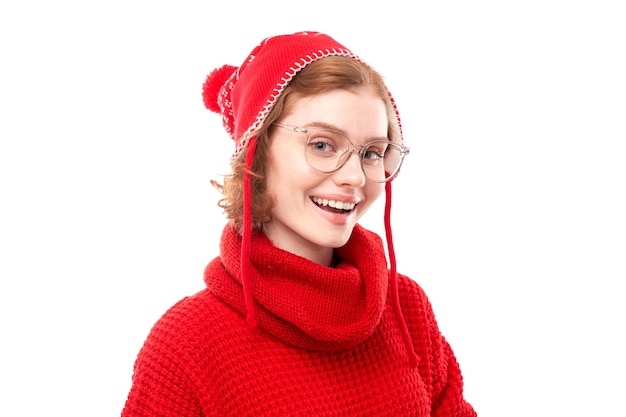 Retrato de uma atraente garota ruiva com suéter vermelho de Natal e chapéu sorrindo alegremente isolado no fundo branco do estúdio