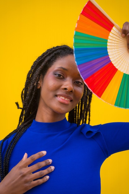 Retrato de uma atraente mulher negra étnica com um fã arco-íris lgbt em um fundo amarelo