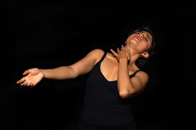 Retrato de uma atriz latina com características indígenas realizando movimentos corporais em um fundo preto