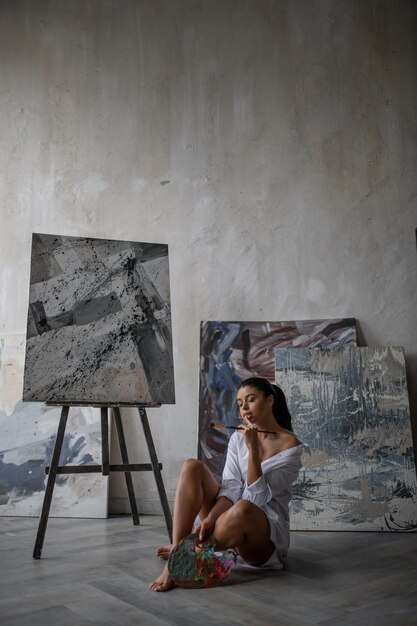 Retrato de uma autêntica garota sexy de raça mista em camisa branca posando contra suas pinturas