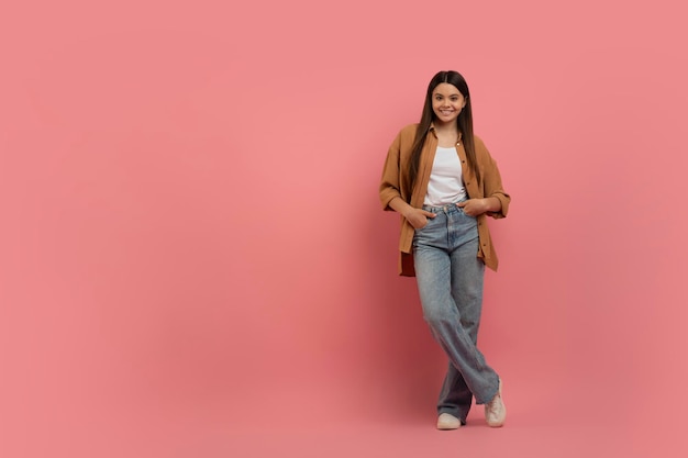 Retrato de uma bela adolescente em roupas casuais de pé em fundo rosa