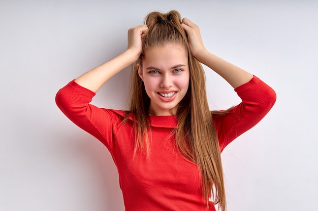 Foto retrato de uma bela adolescente tocando a cabeça isolada no fundo branco, jovem em shir vermelho.