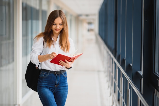 Retrato de uma bela aluna com livros e uma mochila no corredor da universidade