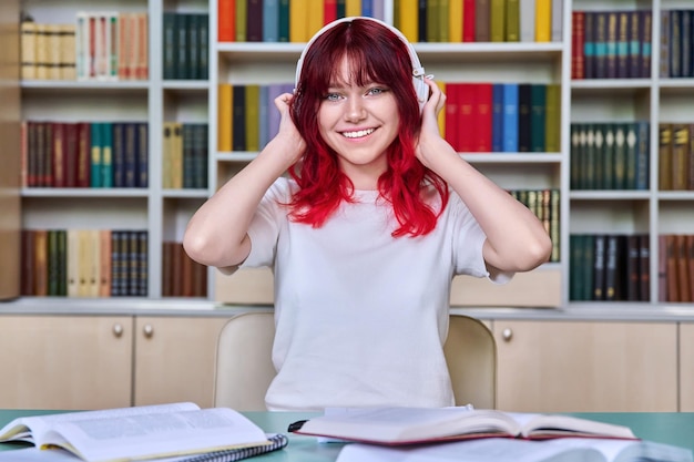 Retrato de uma bela aluna olhando para a câmera sentada na mesa na biblioteca